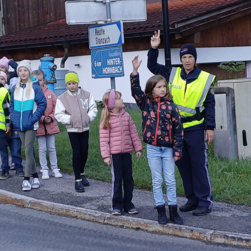 Kind überquert Straße, im Hintergrund stehen die Polizistin und andere Kinder