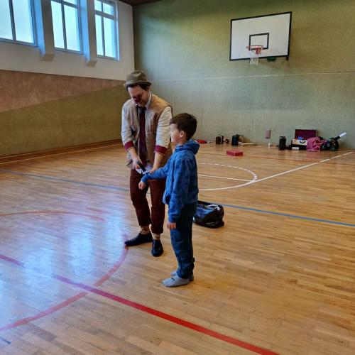 Ein Clown macht einen Zaubertrick mit einem Schüler im Turnsaal