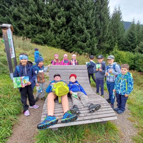 Einige Kinder auf dem Wanderweg, zwei davon liegend auf einer Holzliege