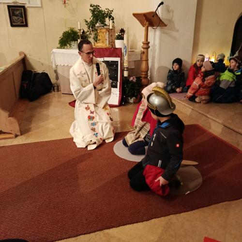 Pfarrer kniend mit Mikrofon befragt zwei Kinder verkleidet als Martin und der Bettler