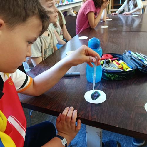 Bub sitz bei Tisch und tropft mit Pipette Wasser auf einen runden Kaffeefilter