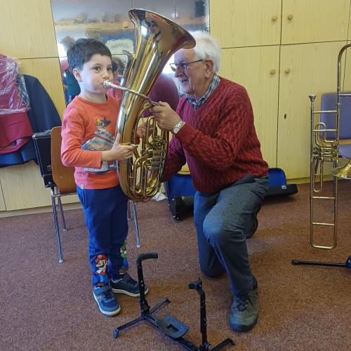 Bub bläst in ein Tenorhorn, ein Mann stützt kniend das Instrument