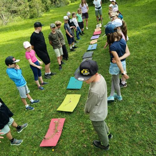Bunte Sitzunterlagen in einer Reihe, Kinder stehen daneben, auf Wiese