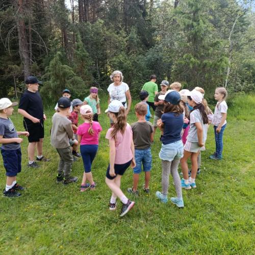 Gruppe von Kindern um die Naturführerin auf einer Wieser, Hintergrund Wald