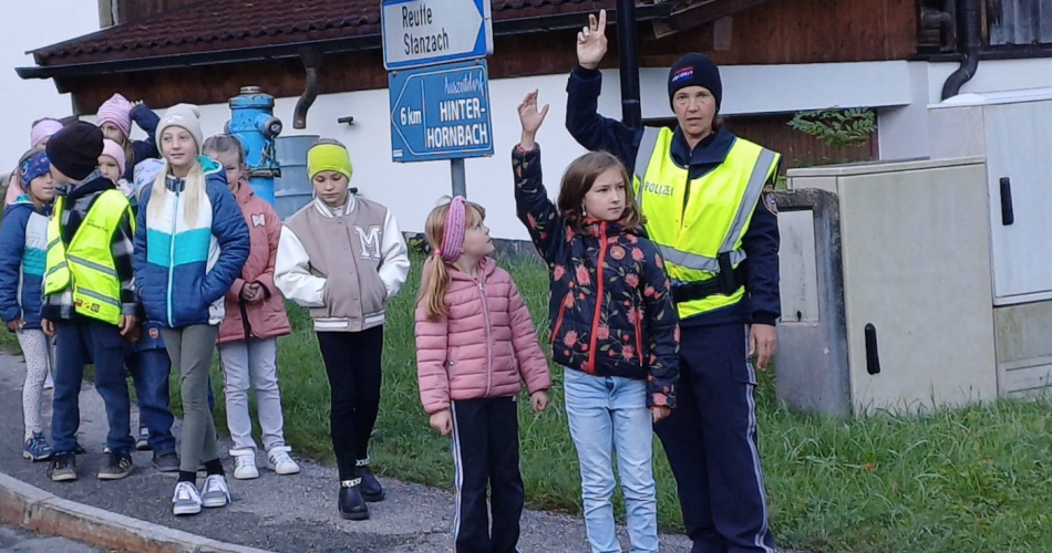 Kind überquert Straße, im Hintergrund stehen die Polizistin und andere Kinder