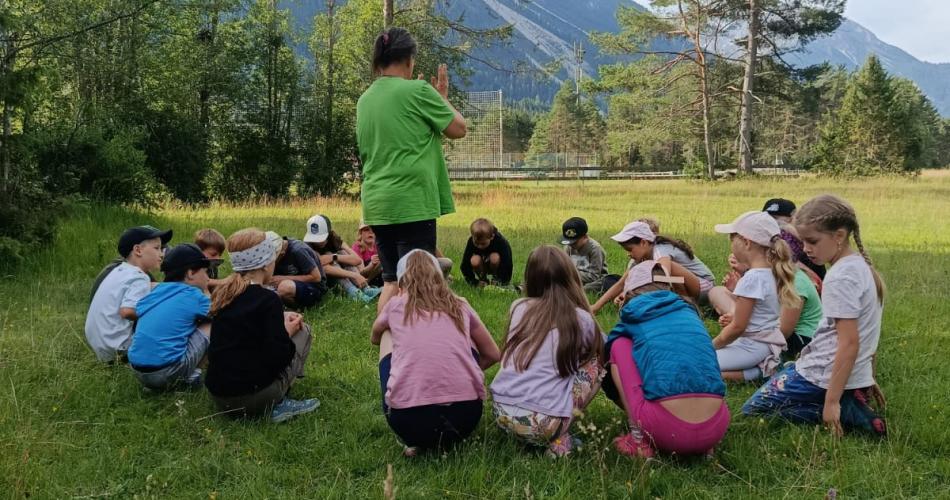 Eine Gruppe von Kindern sitzt im Kreis, in der Mitte steht die Naturführerin
